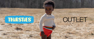 Image of baby wearing tangerine duo wrap and white sweater with rainbow stripes standing in a field