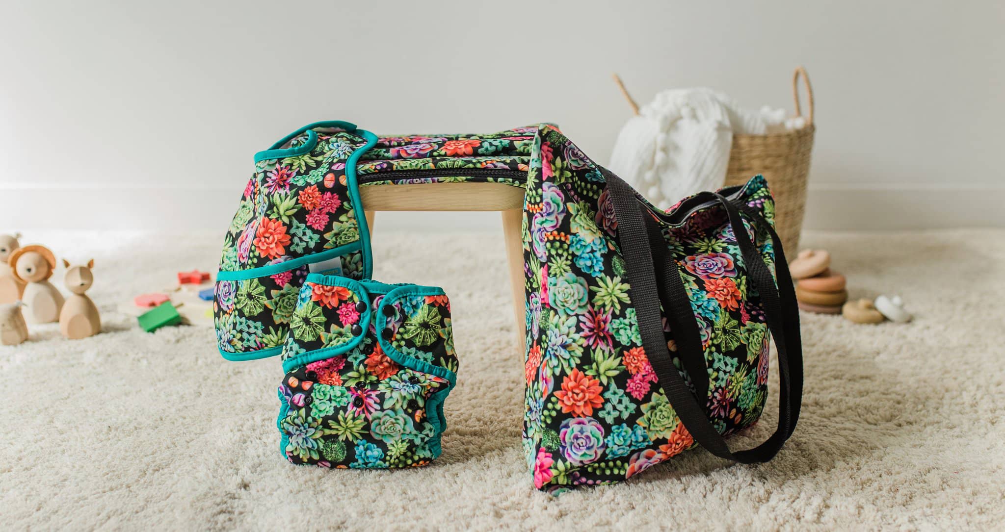 Image of Thirsties Pocket Bib, Pocket Diaper, and Simple Tote Bag in Desert Bloom print in a room with light-colored wall and carpet. 