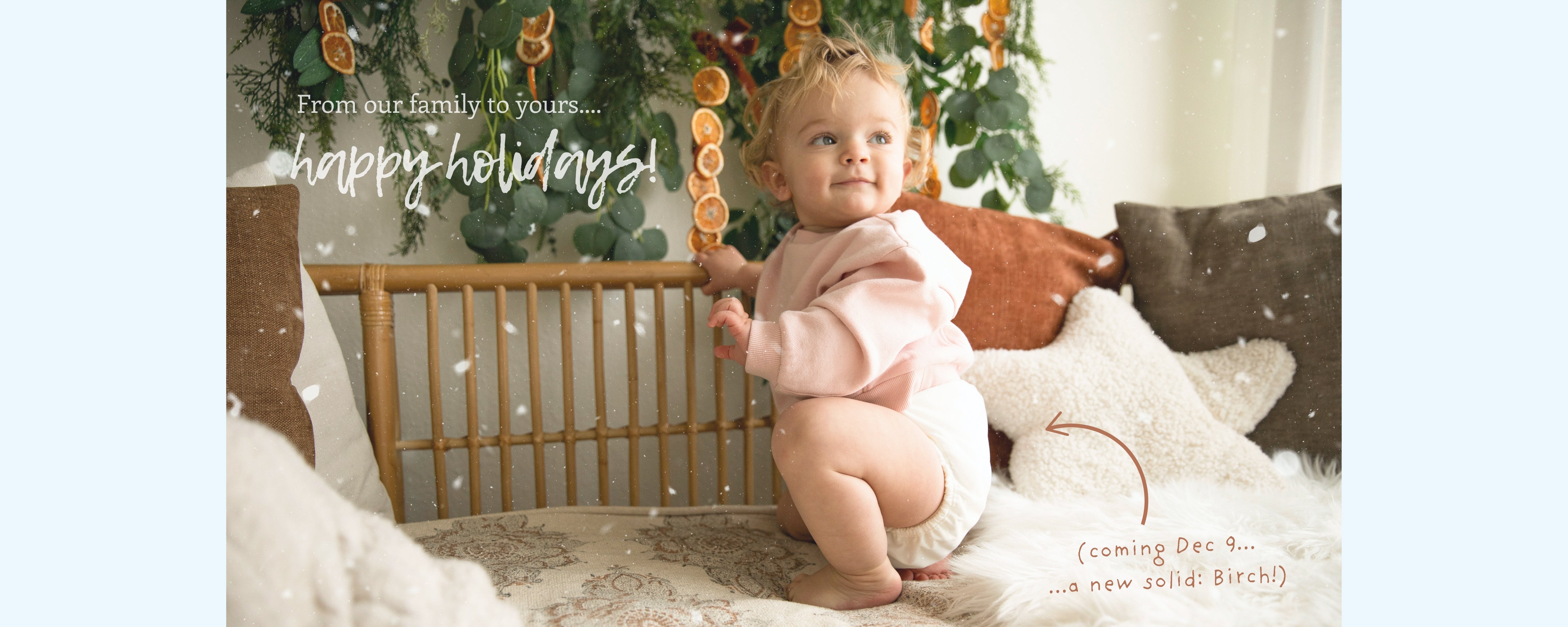 Baby wearing a Thirsties cloth diaper cover in birch sitting in front of a Christmas tree with 'Happy Holidays' text.