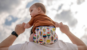 Baby wearing Up and Away Duo Wrap sitting on parent's shoulders