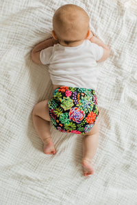 -image of baby wearing desert bloom all in one back view with white shirt one white waffle weave blanket